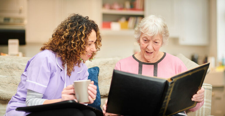 Care nurse sitting with a women looking through a photo album